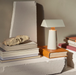 Silk Grey &Tradition MF1 Caret Portable Table Lamp Illuminating a Book with Surrounding Books, Highlighting its Use as a Reading Lamp